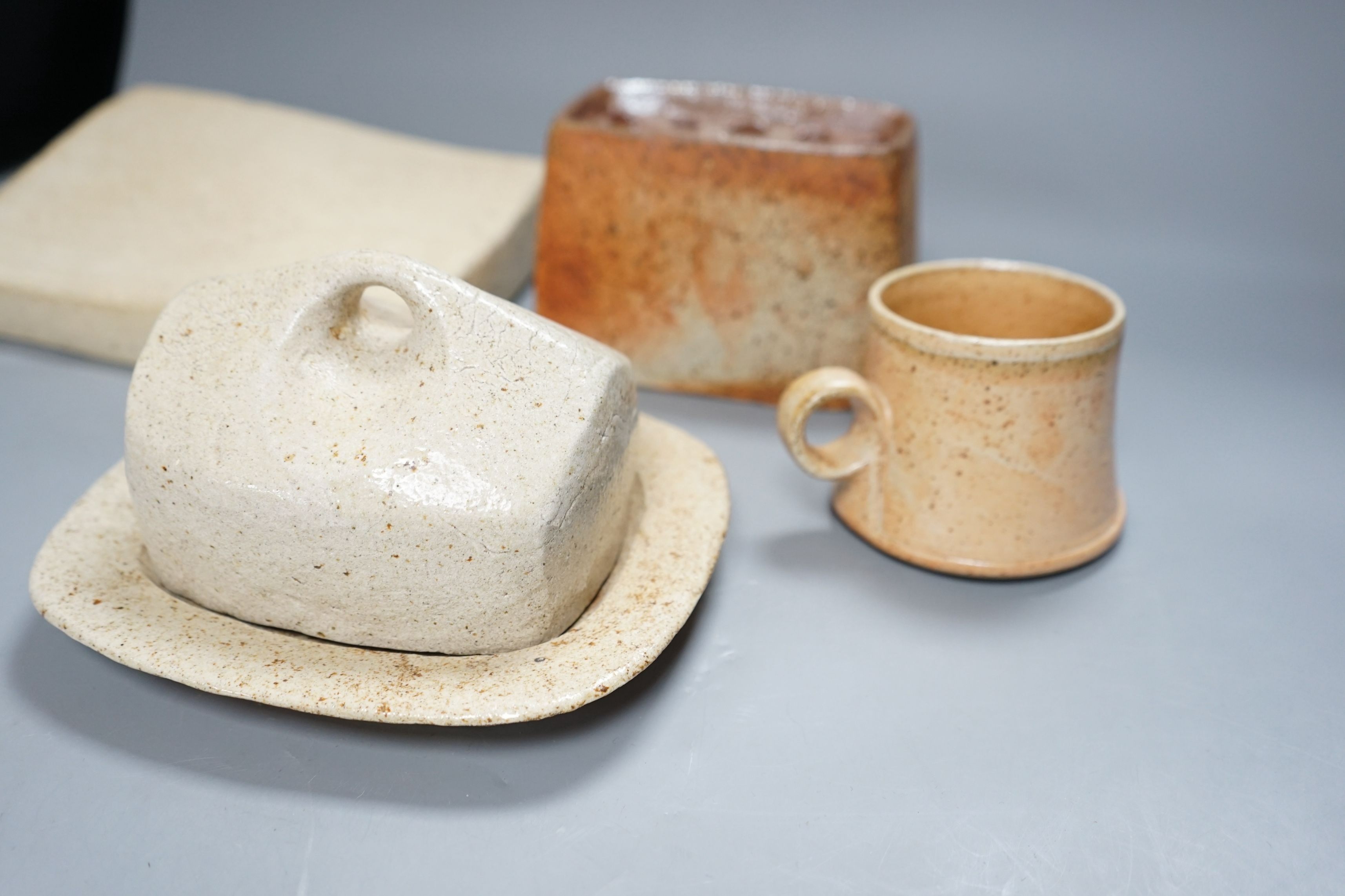 Sarah Walton (b.1945), a salt glazed stoneware flower brick, together with a salt glazed butter dish and cover, a similar mug, and a ‘Field’ horizontally carved linear slab, 22cm wide, all with impressed marks, (4)